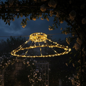 Chapeau, Claudette, ein solarbetriebenes Lichtwesen, hängt abends leuchtend an einem Rosenbogen