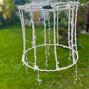 Perl, ein solarbetriebenes Lichtwesen mit zarten Perlensträngen, hängt im Garten